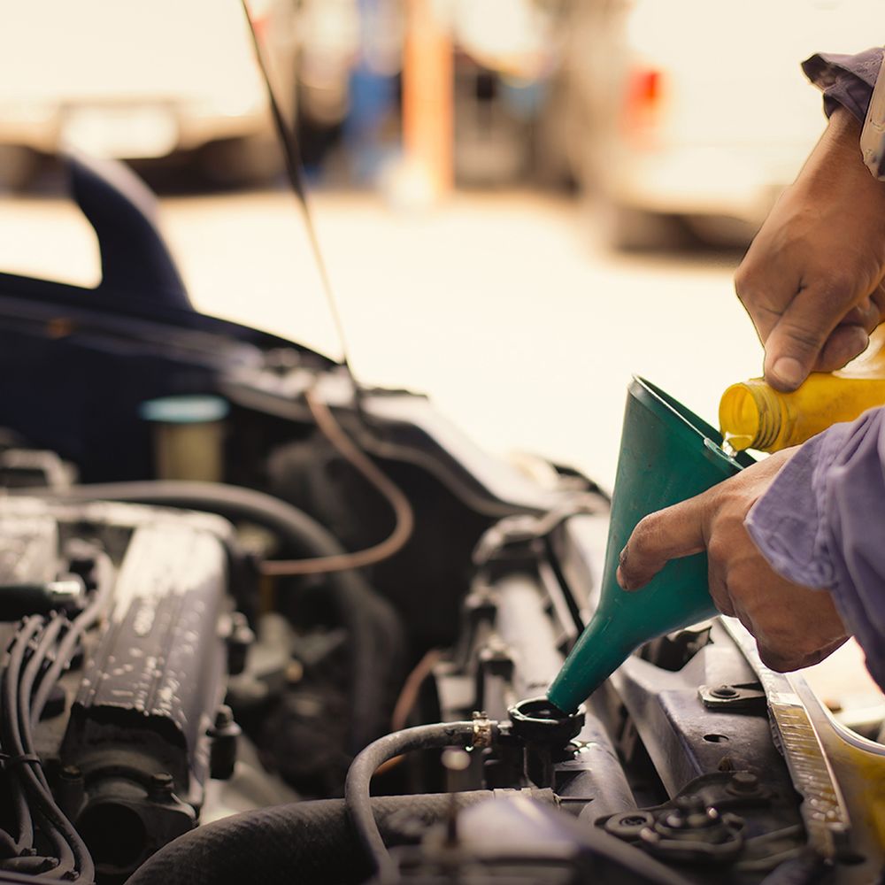 Person pouring oil into a vehicle engine using a green funnel, emphasizing routine oil change services for Volvo maintenance at MB Automotive.