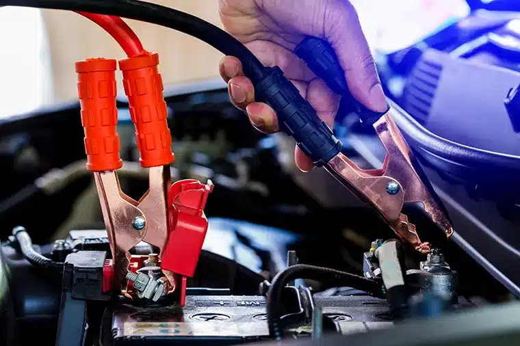 Mechanic using jumper cables to charge a car battery, demonstrating battery charging service at MB Automotive for Volvo vehicles.