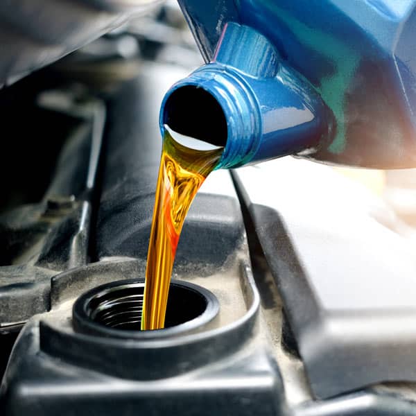 Golden synthetic motor oil being poured into a Volvo engine during routine maintenance.