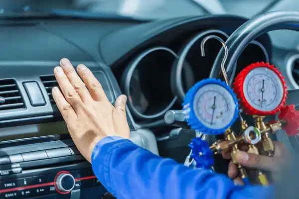 Technician using diagnostic tools on vehicle's climate control system, checking air conditioning performance with pressure gauges.