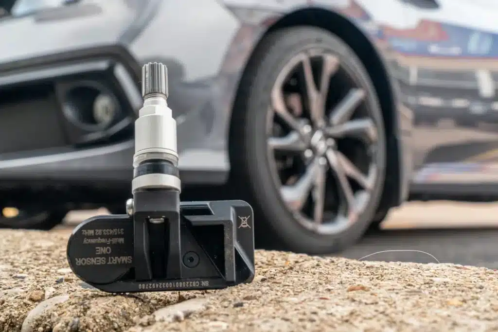 Smart sensor for tire pressure monitoring in front of a vehicle wheel, highlighting car maintenance technology relevant to summer vehicle care.