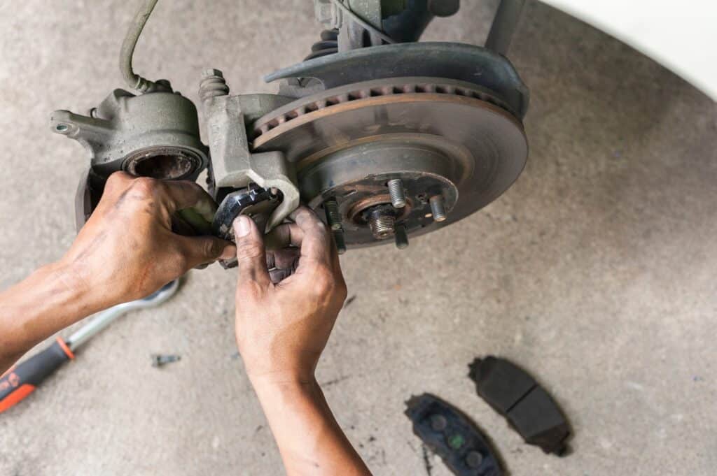 Hands performing brake pad replacement on a vehicle's disc brake system, showcasing worn brake pads and tools, emphasizing brake maintenance and repair services at MB Automotive for Volvo vehicles.