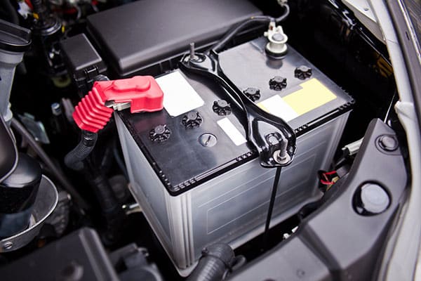 Car battery installed in SUV engine compartment, featuring red terminal clamp, relevant for starting and charging system diagnostics and repair services at MB Automotive.