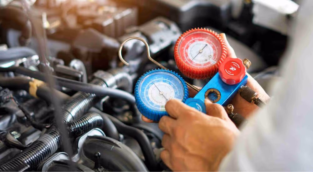 Man holding A/C manifold gauge set, measuring pressure in vehicle's climate control system, highlighting air conditioning diagnostics and repair services at MB Automotive.