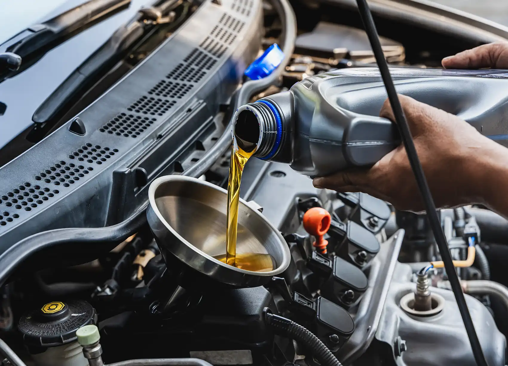Person pouring engine oil into a funnel, demonstrating vehicle maintenance essential for preventing repairs and ensuring reliability.