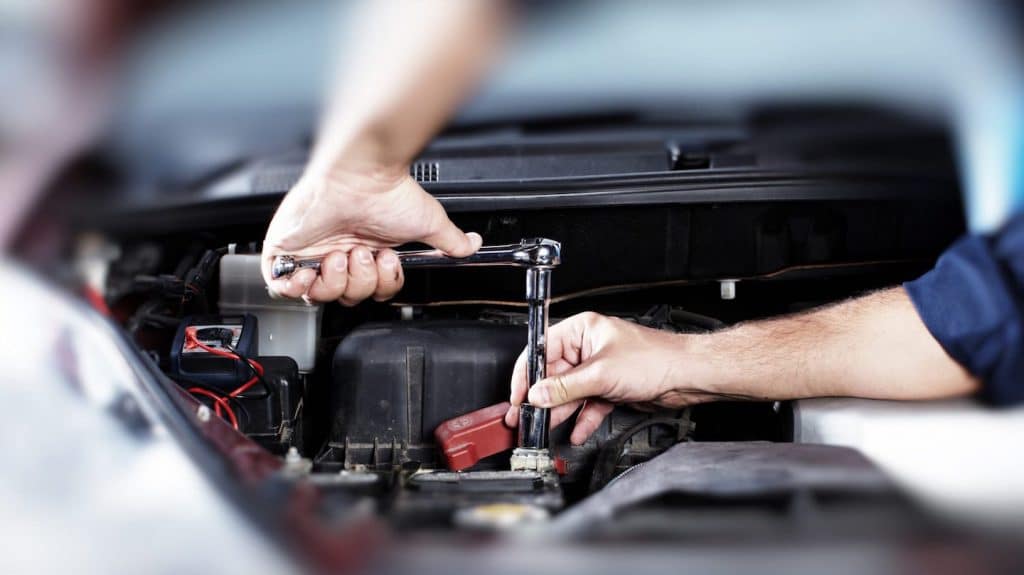 Mechanic using a ratchet wrench to service a BMW battery under the hood, emphasizing electrical system care and maintenance.