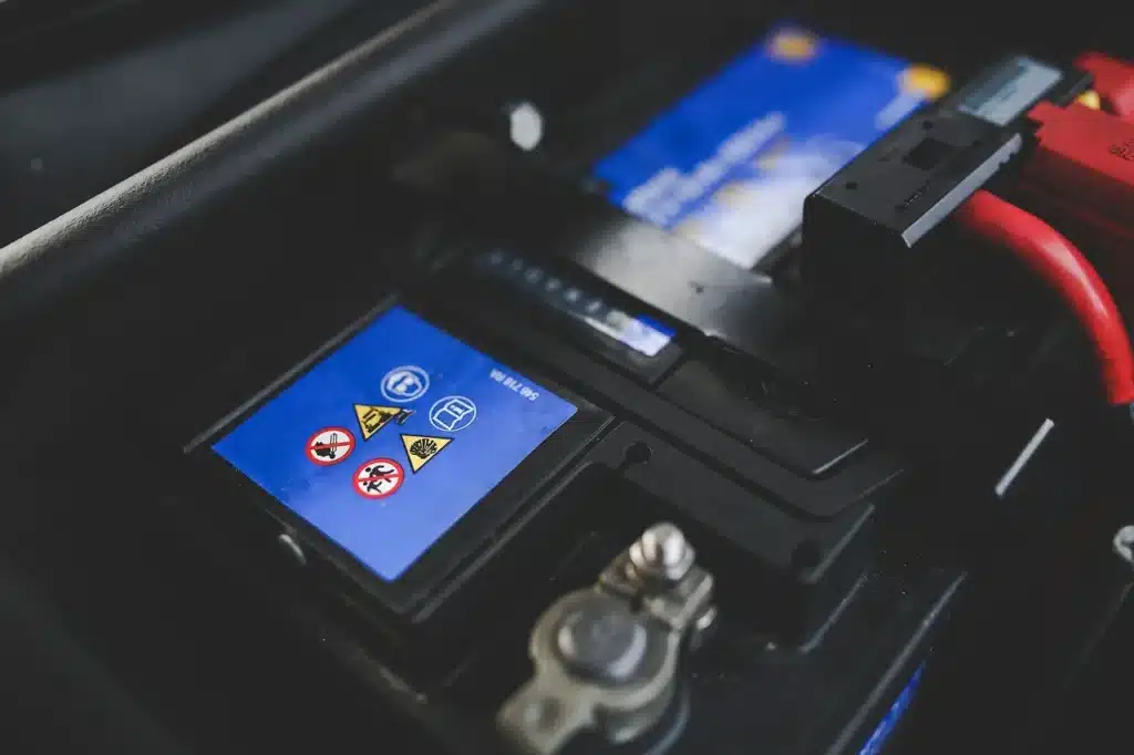 Car battery with warning symbols and red electrical cables