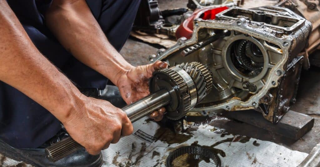 Mechanic repairing a vehicle transmission, focusing on gear assembly and components, in an auto repair workshop.