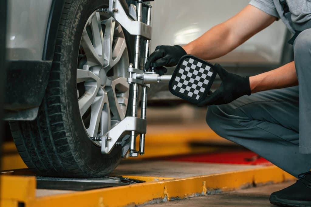 Mechanic adjusting vehicle tire alignment using specialized equipment in an auto repair shop, emphasizing automotive maintenance and safety.