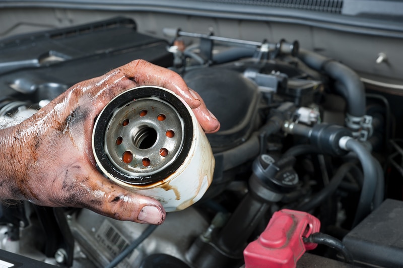 Auto mechanic holding an oil filter with dirty hands, demonstrating routine maintenance in an automotive engine environment.