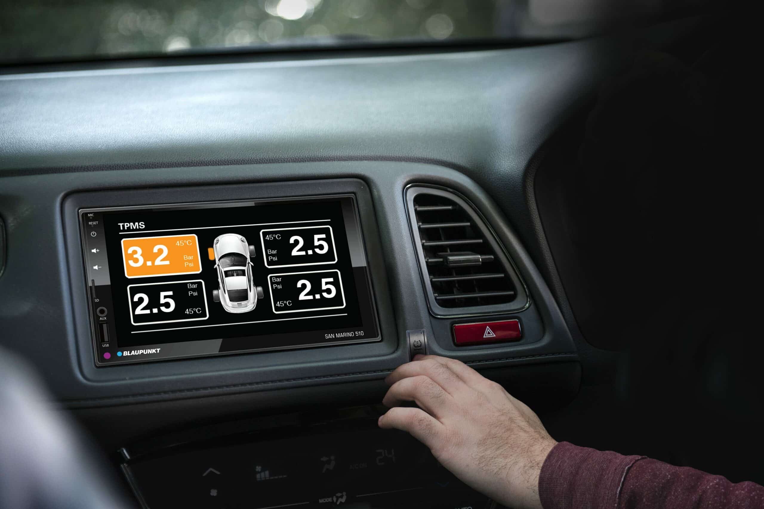 Display screen showing TPMS tire pressure readings with hand adjusting controls in a vehicle interior.