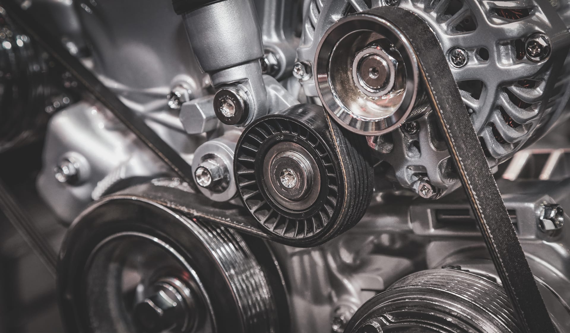 Close-up of car engine components including belts, pulleys, and metallic parts, illustrating the intricate mechanics relevant to transmission systems in vehicles.