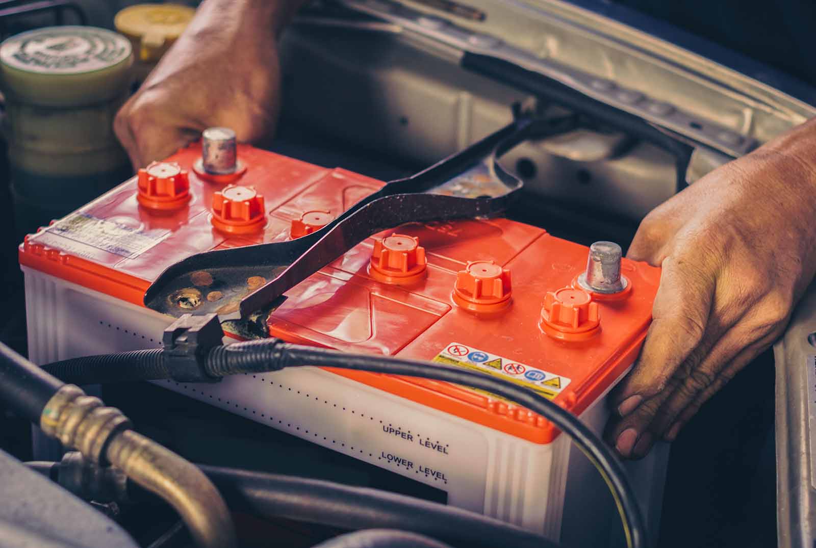 Auto mechanic replacing car battery in vehicle, showcasing battery terminals and tools, emphasizing starting system maintenance services at MB Automotive.
