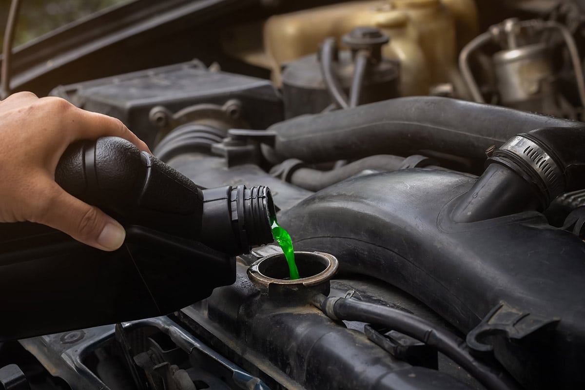 Mechanic pouring green coolant into vehicle radiator, emphasizing essential cooling system maintenance for optimal engine performance.