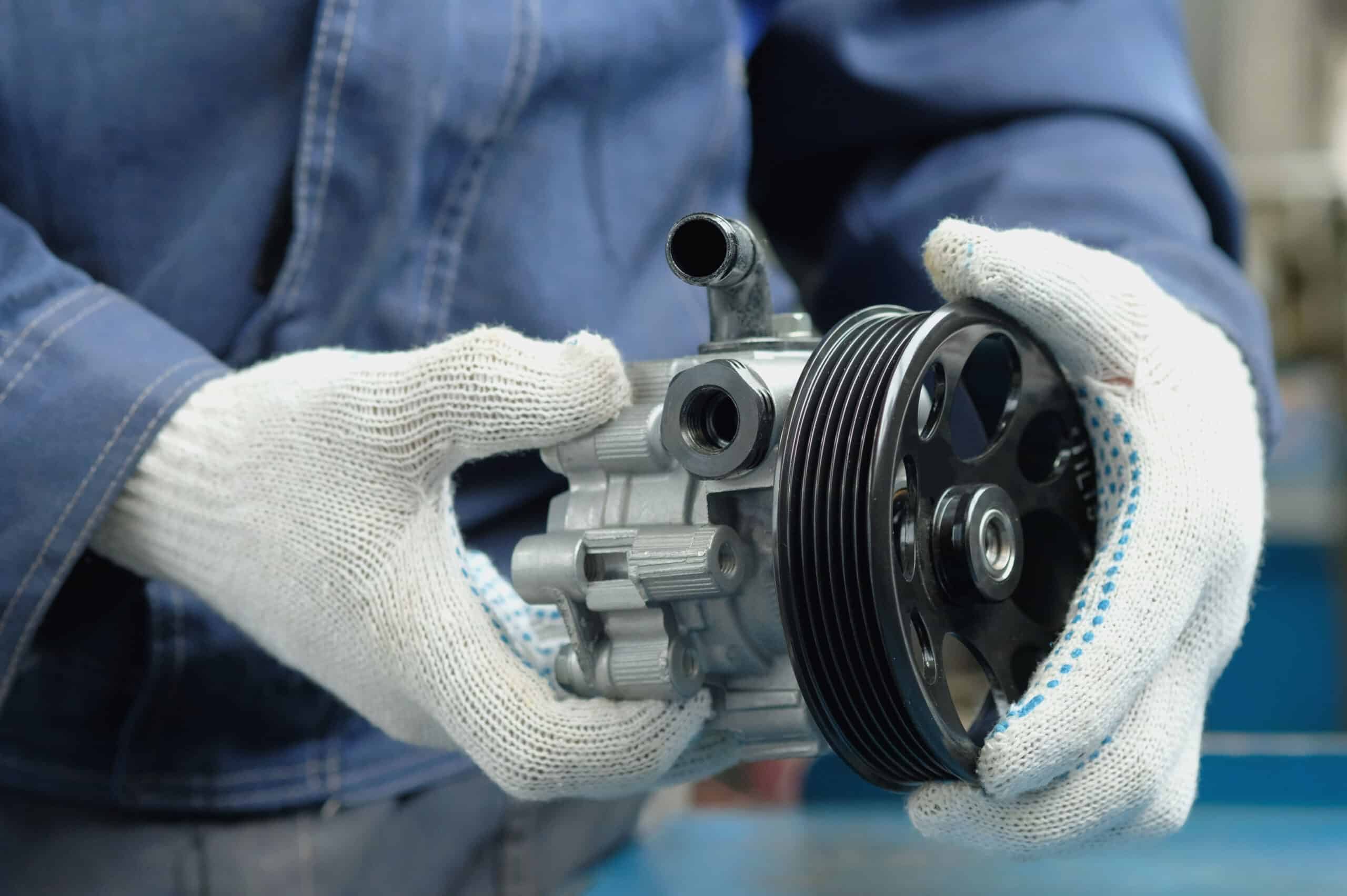 Technician holding a covered power steering pump, highlighting essential vehicle steering system components for maintenance and repair services at MB Automotive.