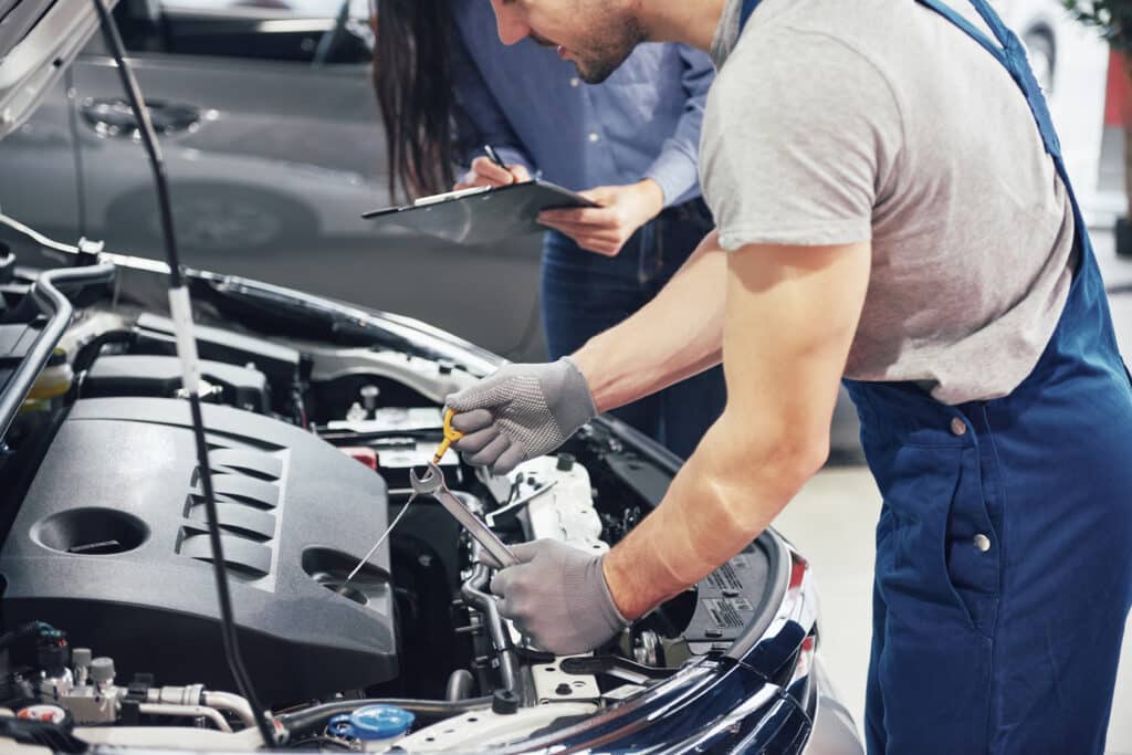 man mechanic woman customer look car hood discuss repairs scaled