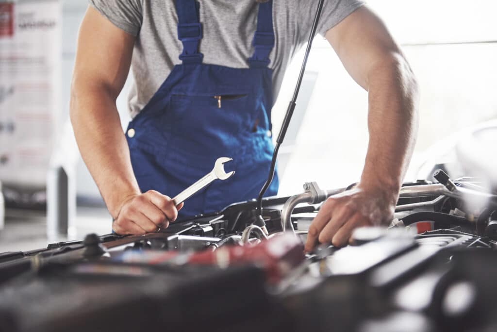 Muscular car service worker repairing vehicle engine with wrench in auto repair shop in Bay Shore.