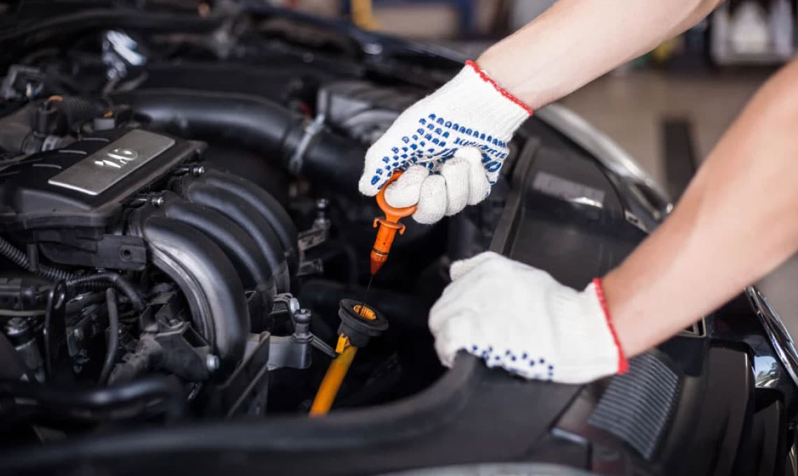 Mechanic checking engine oil level with dipstick in auto repair shop, highlighting expertise in vehicle maintenance for European and domestic cars.