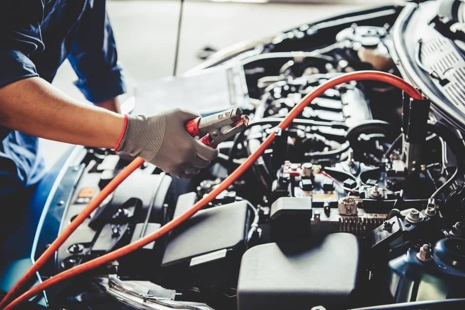 Mechanic using jumper cables on a car battery, performing electrical system diagnostics and repairs, emphasizing Volvo electrical maintenance services.