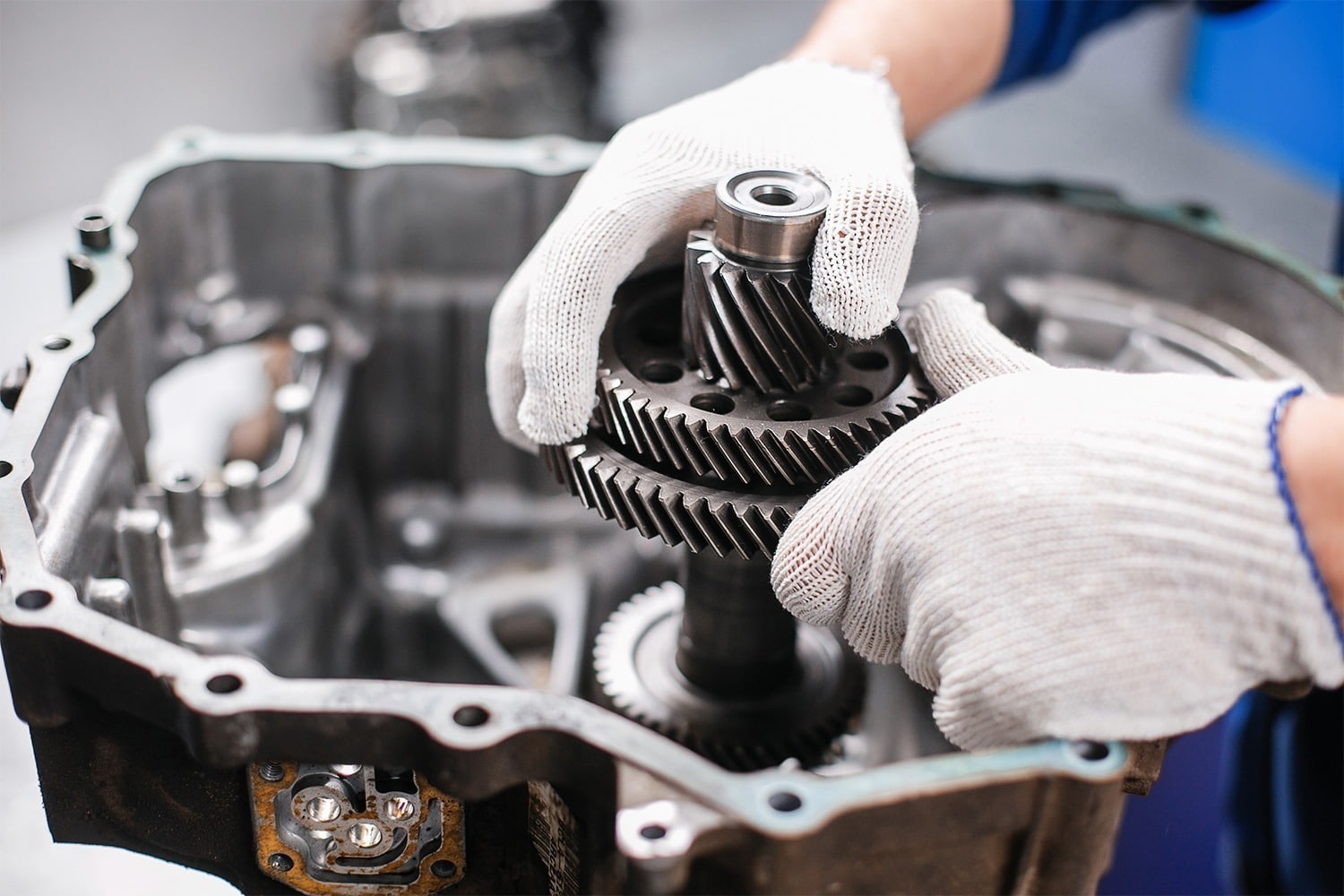 Mechanic repairing transmission gears with gloves, focusing on precision gear assembly in a vehicle transmission system.