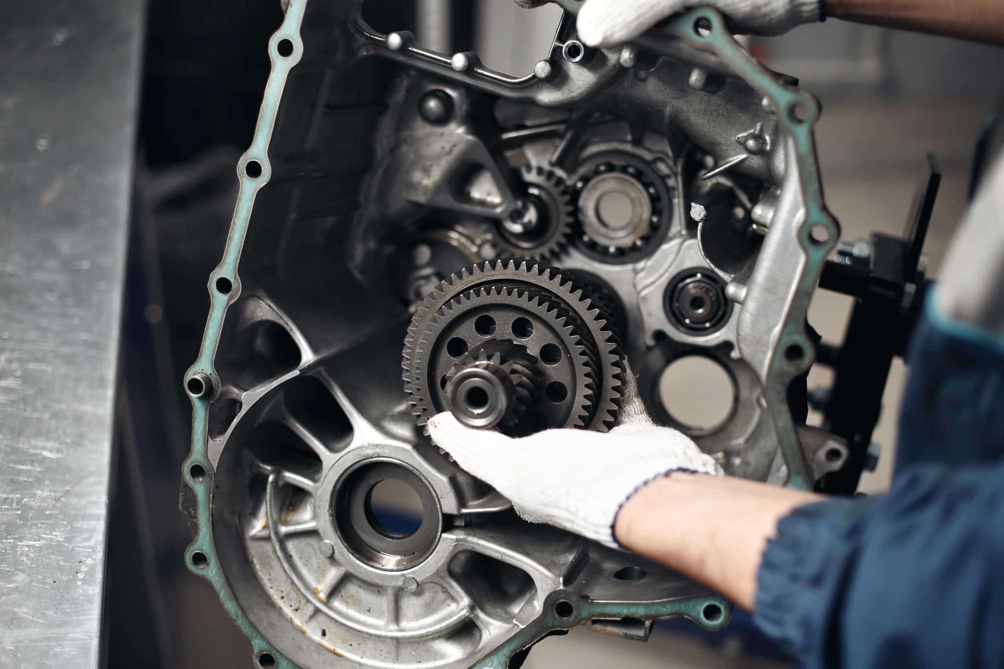 Mechanic holding gear inside a disassembled transmission, illustrating automotive repair processes relevant to avoiding car repair scams in Suffolk County.