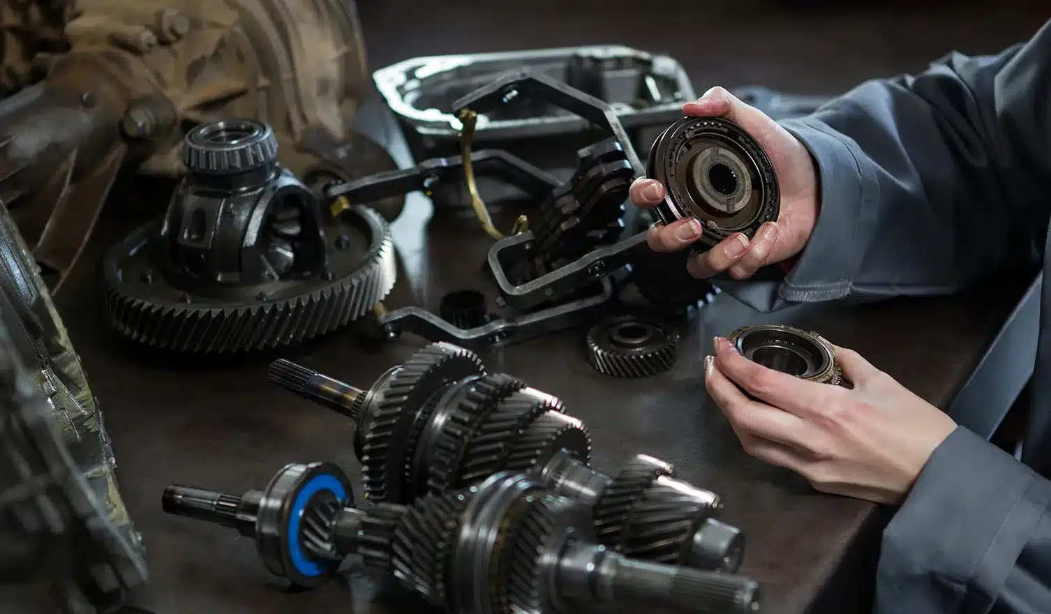 Hands inspecting transmission components, including gears and seals, on a workbench, showcasing the intricacies of transmission repair relevant to vehicle maintenance.